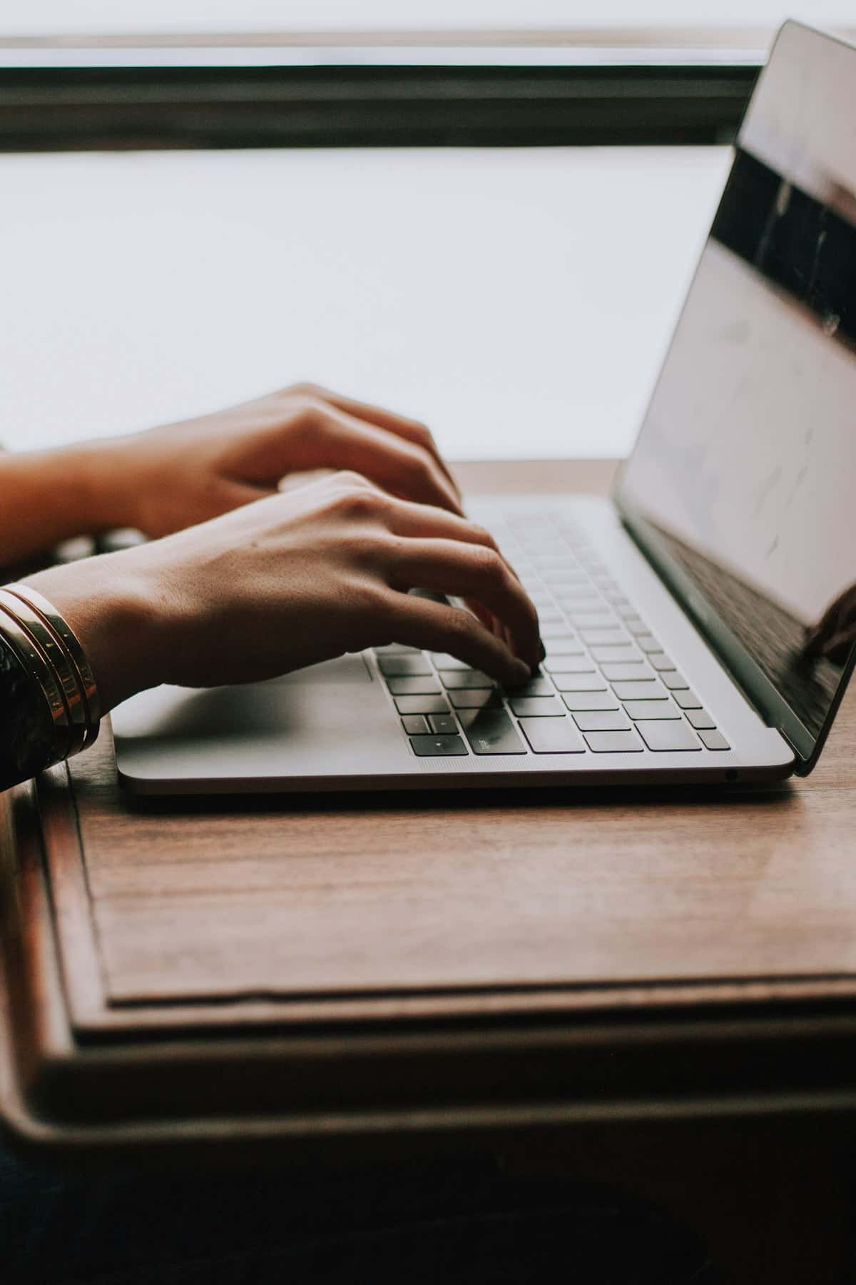 Hands typing on a laptop at a wooden desk